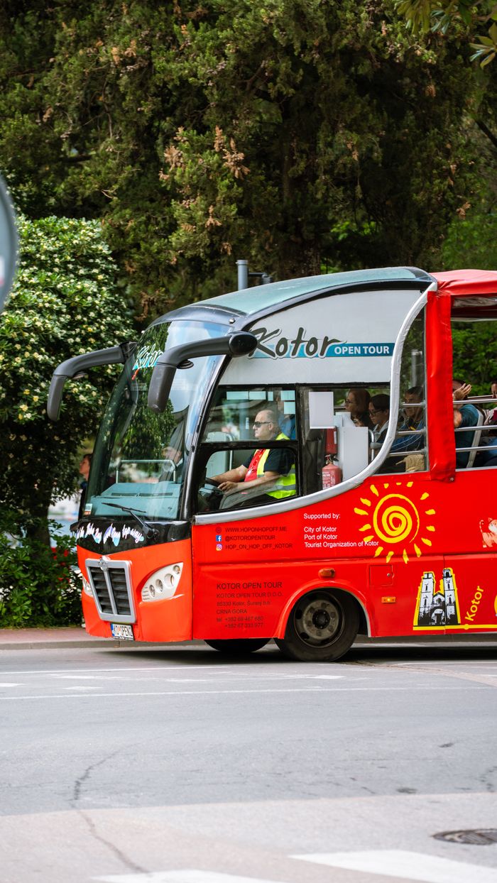 Red open tour bus in Kotor, Montenegro, showcasing scenic travel opportunities.